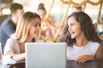 Two beautiful young women looking at laptop and laughing at bar