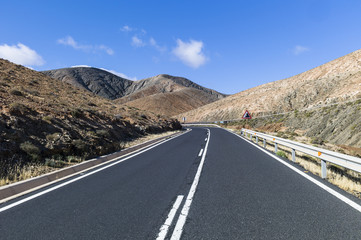 Classic mountain road with white guardrail winding up the volcano hills of Fuerteventura Canary Islands Spain.
