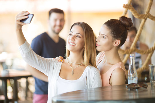 Two beautiful young women taking selfie at bar