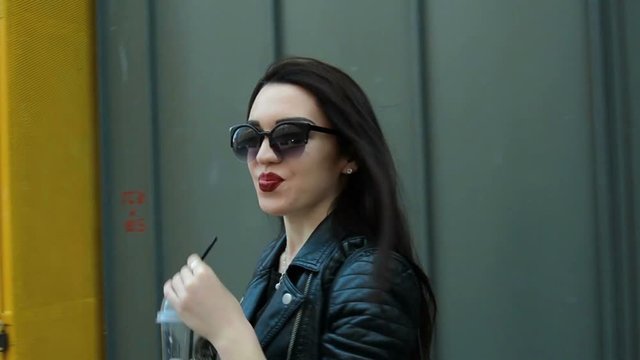 beautiful young girl in sunglasses goes around town smiling and drinking a beverage
