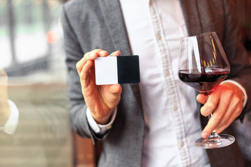 Young businessman shows business card in restourant with glass of red wine