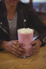 Mid section of woman with milkshake glass in cafe
