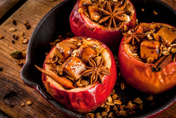 Autumn food recipes. Baked apples stuffed with granola, toffee and spices. On black stone table, in...