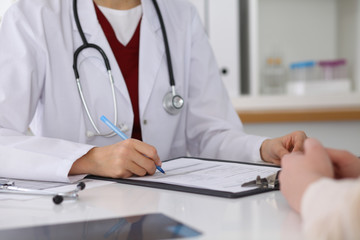 Close up of a female doctor filling up  an application form while consulting patient