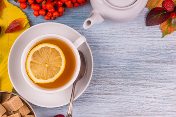 cup of tea with lemon on old wooden table with rustic leaves of autumn, cane sugar cubes in a metal cup. copy space