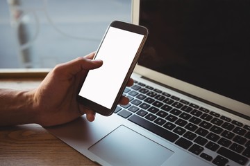 Cropped hand of man using phone over laptop