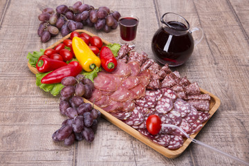 Set of meat delicatessen, tomatoes and peppers, wine on a wooden table.