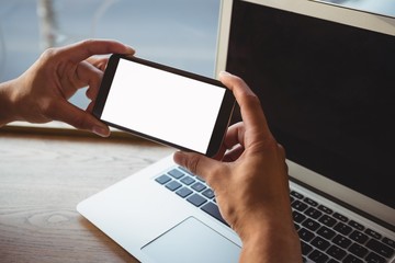 Cropped hand of man holding phone over laptop