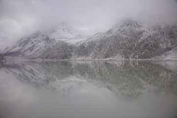 Fototapeta na wymiar snow-civered Altai mountains reflect in Akkem lake on a cloudy day; Russia