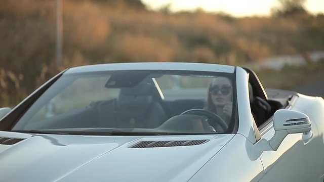 beautiful sexy girl with long hair in a leather jacket and leather pants in sunglasses sits in a cabriolet