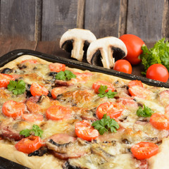 Homemade pizza with tomatoes, mushrooms, sausage and cheese over wooden background