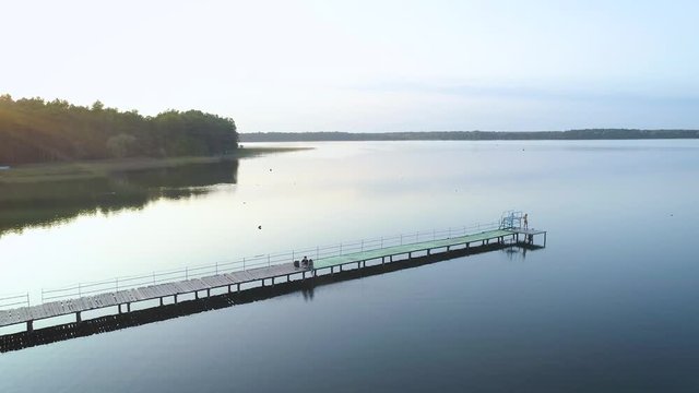 4K Aerial footage. Fly out pier on calm lake at sunset