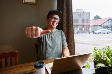 man smiling and laughing while giving a thumbs up next to computer