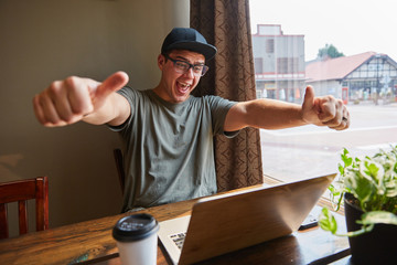 man smiling and laughing giving two thumbs up next to computer at coffee shop
