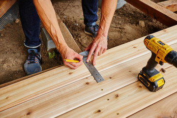 man drilling and measuring wood for deck - Powered by Adobe