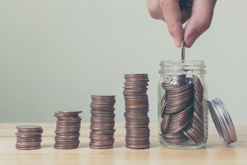 Hand of male or female putting coins in jar with money stack step growing growth saving money, Concept finance business investment