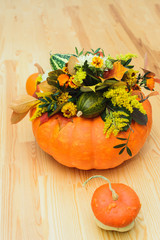 autumn bouquet of decorative pumpkins, flowers and leaves in a vase of orange pumpkin on a wooden table
