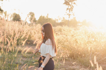 Young woman standing in forest and bush in sunny rays field at sunset in summer meadow.Are looking at grass field.