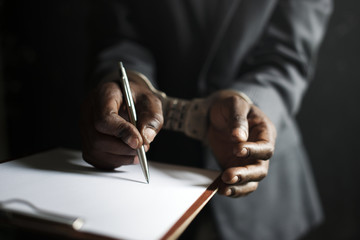 Closeup of hands cuffed forced to sign paper - obrazy, fototapety, plakaty