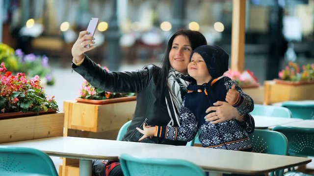 A young mother makes selfie with her little cute son at a table in a cafe