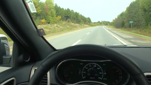 DRIVER'S POV: Driving on empty highway trough beautiful autumn forest with red, yellow and green trees. FPV autonomous car self steering on empty countryside road past colorful forest trees in fall