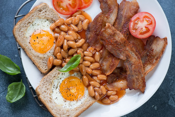 Closeup of english breakfast with fried bacon, eggs in the basket and beans in tomato sauce, flat-lay