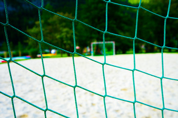 Green net close up from behind view with blur background of sand field and another side goal