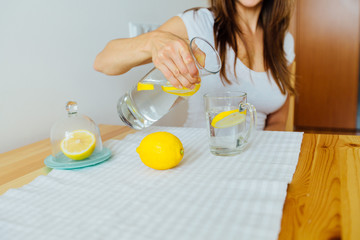 Drink water. Woman's hand pouring fresh pure water with pieces of lemon from pitcher into glass in...