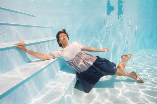young woman in blue and white dress swim and dive underwater floating pool with transparent water in Beautiful Mysterious Underwater World. Fantastic Fairy dreamy fashion. Water safety class