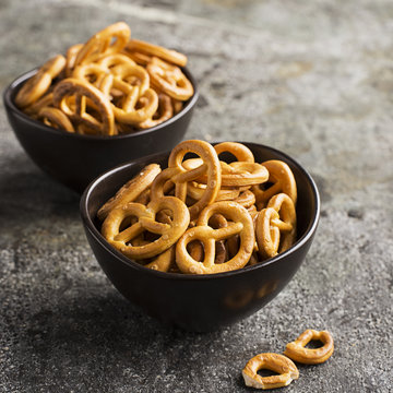 Salted pretzels in two ceramic matte dark bowls on a gray stone grunge background. Selective focus.