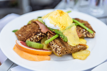 Egg Benedict with seven grain bread with sliced of orange and asparagus at restaurant in Dubai.