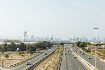 Main road with desert and electricity posts and silhouette buildings in background at Dubai. 