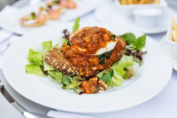 Egg Benedict with tomato stew sauce on seven grain bread with iceberg lettuce salad at restaurant in Dubai.