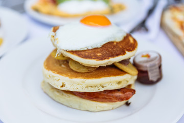 Pancakes with deep fried bacon, fried potato with peel and fried egg on the top served with maple syrup at restaurant in Dubai.