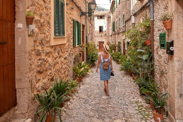 Beautiful pretty woman walking at old town pavement street with flowers and looking away. Travel concept