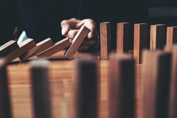 Close up of businessman hand Stopping Falling wooden Dominoes effect from continuous toppled or...