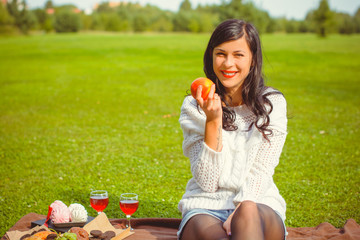 Nice young woman with apple at a picnic in the park sit on green grass. Consent of good health lifestyle and harmony with her body