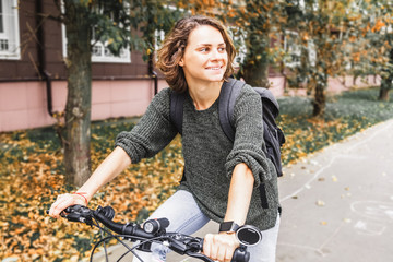 Beautiful young female student in a sweater and jeans on a bicycle on an autumn street