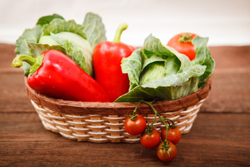 Basket with fresh vegetables on a wooden table. Tomatoes, Bulgarian pepper and cabbage.