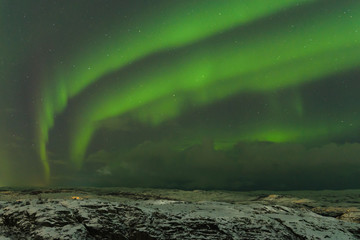 Aurora and clouds in the night sky in winter over the tundra and hills.