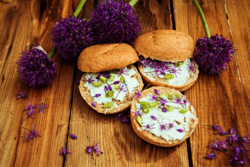 Toasted bread bruschetta with cream cheese and garlic edible flowers on olive wooden cutting board on stone slate gray background. Top view