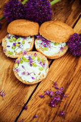 Toasted bread bruschetta with cream cheese and garlic edible flowers on olive wooden cutting board on stone slate gray background. Top view