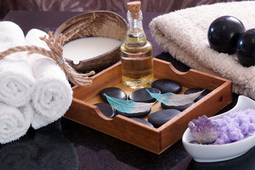 Fototapeta na wymiar White towels knitted next to the set for massage from Bian stones, aroma oil and violet salt, in a wooden box a set of hot stones for relaxation and for a spa massage.