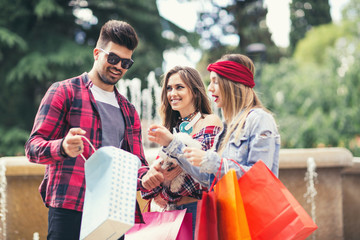 Three friends holding colored bags in hand on the way to the Mall for shopping