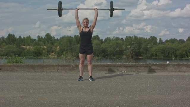 Young fitness woman working out with barbells outdoors