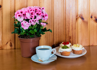 Cup of coffee, sweet cakes and pelargonia flower on wooden table