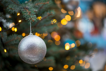 Close-up detail of a glittery Christmas ornament hanging from the branches of a spruce tree, with bokeh lights in the background, Singapore. Shallow focus. Xmas and festive holidays concept.