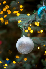 Close-up detail of a glittery Christmas ornament hanging from the branches of a spruce tree, with...