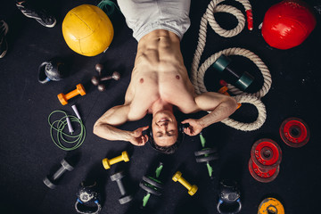 man lying with rope in gym between fitness accessories and listening music