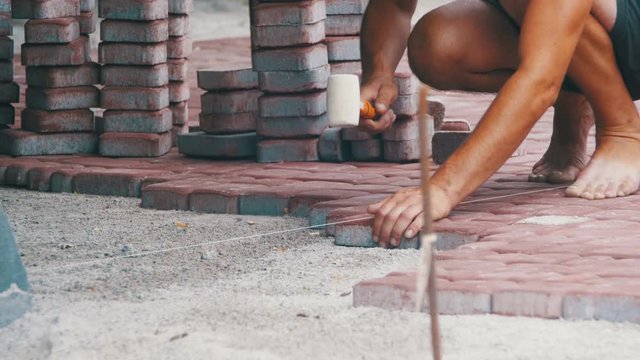 Worker is Laying Paving Stones using Hammer. Construction site, worker installing concrete brick pavement, using hammer.